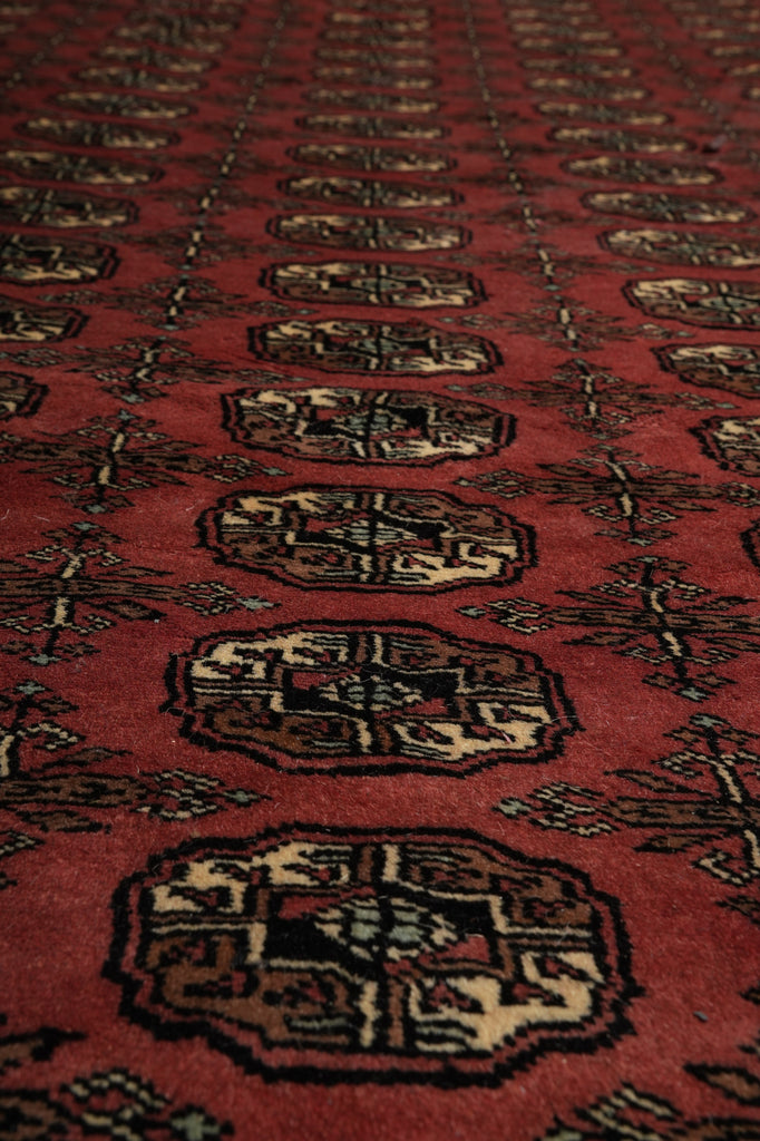 A close-up of a red patterned rug with repeating octagonal medallions and floral motifs in beige, black, and brown.