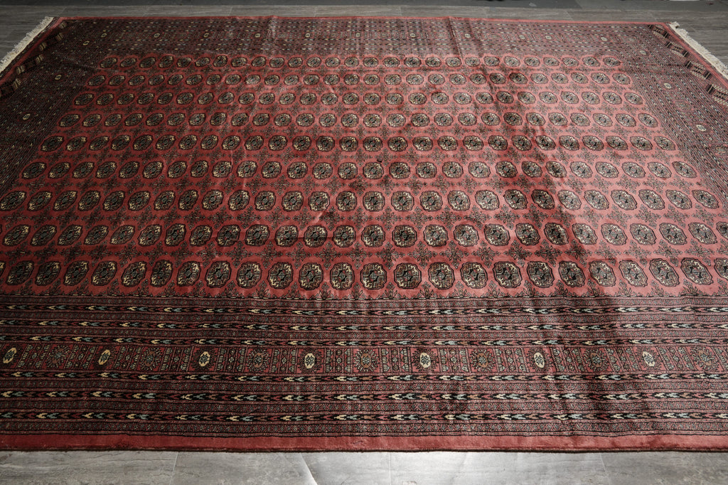 A large traditional oriental rug with a red field, featuring rows of circular medallions and a patterned border, laid out on a gray tiled floor.