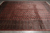 Load image into Gallery viewer, A large traditional oriental rug with a red field, featuring rows of circular medallions and a patterned border, laid out on a gray tiled floor.