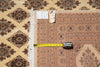 Load image into Gallery viewer, A patterned area rug shown folded with a tape measure laid across it to indicate size. The rug has a beige, brown, and rust-orange geometric design with white fringe.