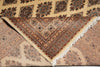 Load image into Gallery viewer, A close-up of a patterned area rug with a triangular section folded over to show the underside and fringe. The rug features intricate geometric and floral motifs in beige, brown, and muted red tones.