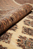 Load image into Gallery viewer, A close-up of a patterned area rug with a rolled section showing the pile and detailed design. The rug has a warm beige base with brown, rust, and black geometric motifs.