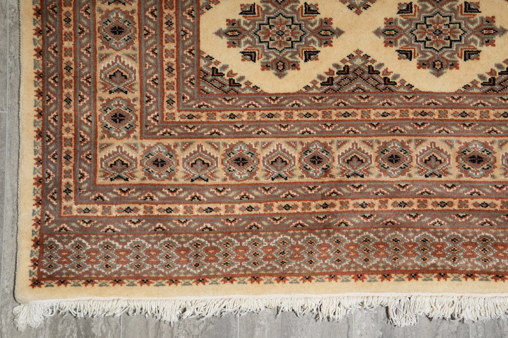 A close-up of a patterned area rug showing its corner, detailed geometric borders, and white fringe on a gray floor.