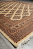 Load image into Gallery viewer, A close-up of a patterned area rug with cream, rust red, and brown tones, showing its detailed geometric design and fringed edge on a gray floor.