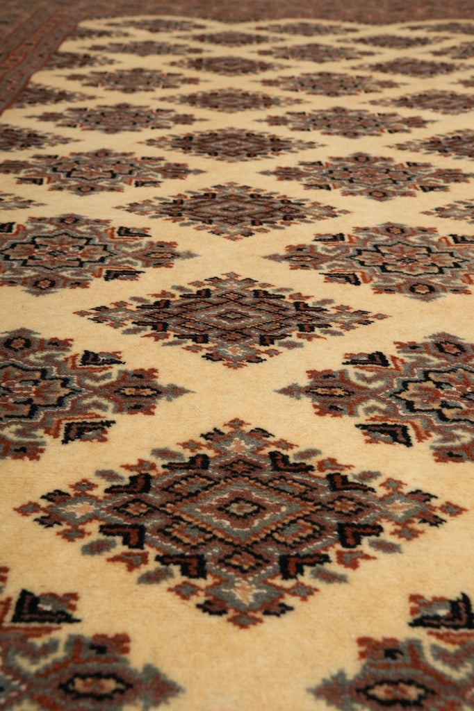 A close-up of a patterned rug with repeating diamond motifs in beige, brown, black, and muted blue-gray tones.