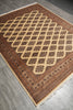 Load image into Gallery viewer, A rectangular area rug with a traditional Persian-style geometric pattern, featuring a large diamond lattice in the center and detailed borders. The rug has a warm brown and beige color palette with white fringe on the ends, shown laid out on a gray wood floor.