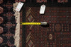 Load image into Gallery viewer, A patterned area rug with dark navy, red, and beige geometric designs and cream fringe, shown with a yellow tape measure and white tags on a dark background.