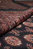 Load image into Gallery viewer, A close-up of a folded area rug showing its detailed pattern and pile texture. The rug features a dark charcoal black base with intricate traditional motifs in rust red, beige, and brown.
