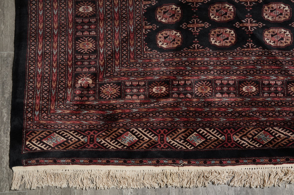 A close-up of a traditional patterned rug showing its detailed border, geometric motifs, and cream-colored fringe at the bottom.