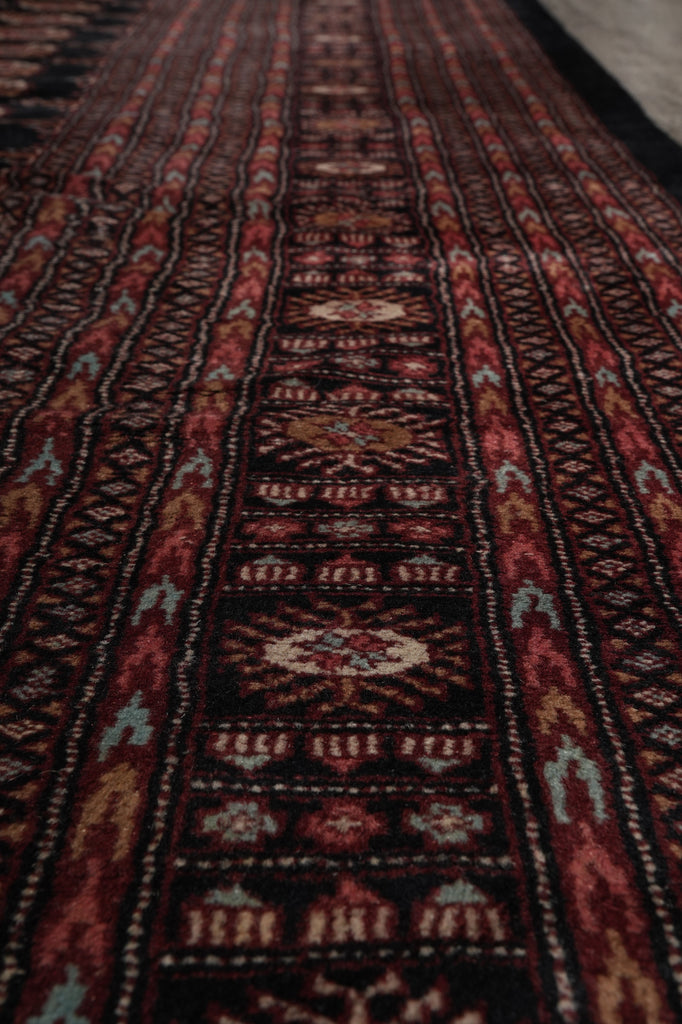 A close-up view of a patterned rug showing detailed woven geometric and floral motifs in dark red, black, brown, and cream.