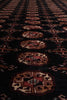 Load image into Gallery viewer, A close-up of a dark patterned rug or textile with repeating ornate medallion motifs in red, beige, and brown on a black background.