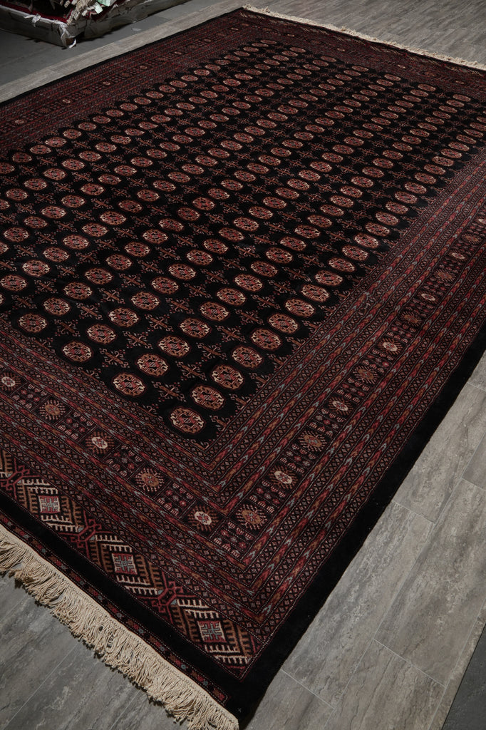 A traditional Persian-style area rug with a dark red and black background, featuring circular medallion motifs and a beige fringed edge, shown laid out on a gray tiled floor.