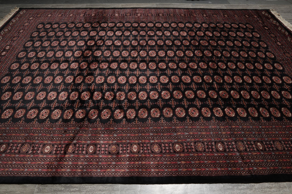 A large rectangular area rug with a dark black field, featuring rows of repeating circular medallion motifs in red and brown, and a detailed patterned border.