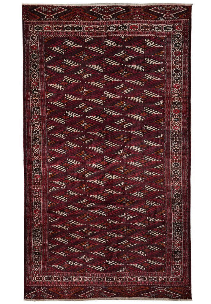 A traditional Persian-style area rug with a deep red field, geometric diamond patterns, and a detailed multi-colored border.