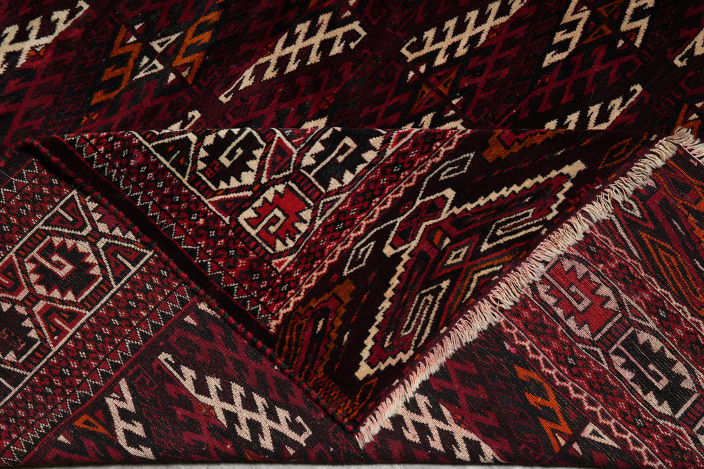 A close-up of a folded patterned rug with geometric tribal designs in deep red, black, cream, and brown tones.