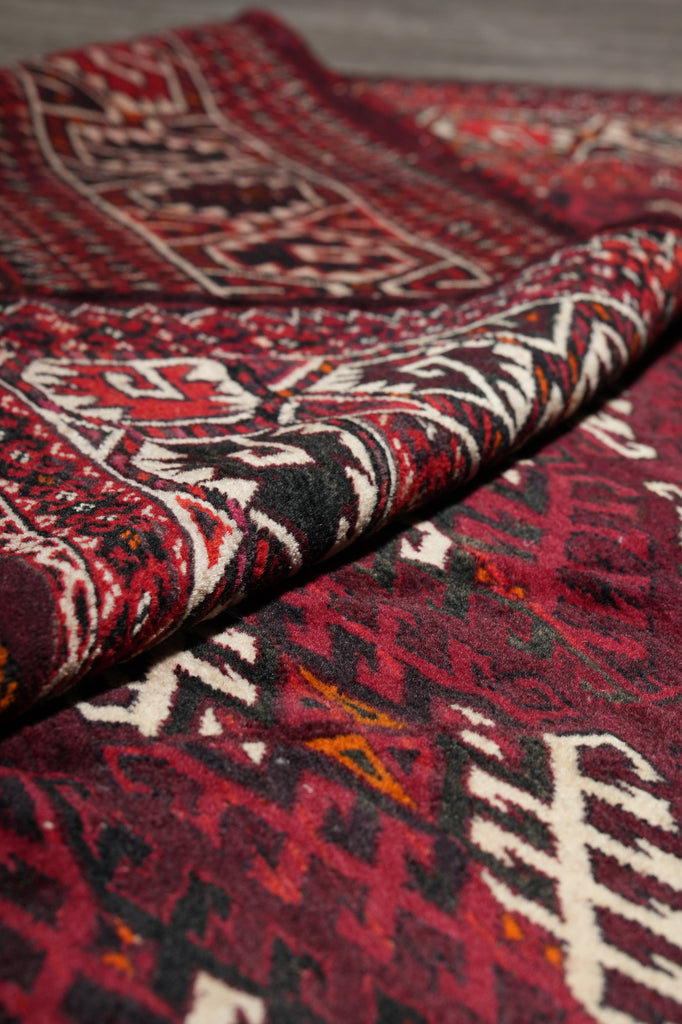 A close-up of a folded patterned textile, likely a rug or throw blanket, showing a deep red, black, and cream geometric tribal design.