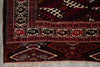 Load image into Gallery viewer, A close-up of a patterned rug corner showing geometric and tribal-inspired motifs in deep red, black, beige, and brown, with fringed edges visible at the bottom.