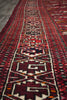 Load image into Gallery viewer, A close-up view of a traditional patterned area rug with a geometric design in red, black, cream, and orange, laid out on a gray floor.