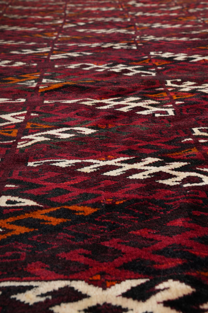 A close-up of a woven textile with a bold geometric pattern in deep red, black, cream, and orange.