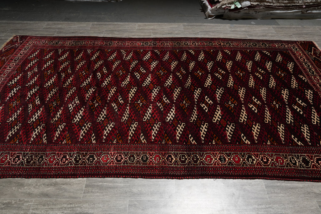 A long rectangular area rug with a deep red and black geometric pattern and a decorative border, laid out on a gray tiled floor.