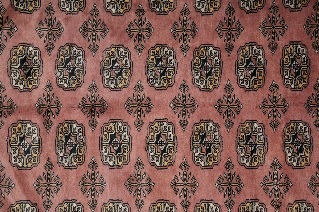 A close-up of a patterned textile or rug with a dusty pink background and repeating ornate medallion motifs in black, beige, and muted gold.