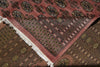 Load image into Gallery viewer, A close-up of a patterned area rug with a dusty rose pink field, intricate black, brown, and gold geometric motifs, and white fringe on one corner, laid over another matching rug.