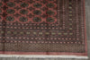 Load image into Gallery viewer, A close-up of an oriental rug showing its detailed pattern, featuring a dusty rose field with black, gold, and beige motifs, a dark patterned border, and white fringe at the bottom.