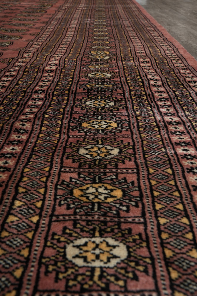 A close-up view of a patterned area rug with a dusty rose and dark brown base, featuring traditional geometric motifs in black, yellow, and cream.