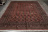 Load image into Gallery viewer, A large rectangular area rug with a traditional pattern, featuring a dusty red field, dark brown borders, and repeating medallion motifs in black and beige, laid out on a gray wooden floor.