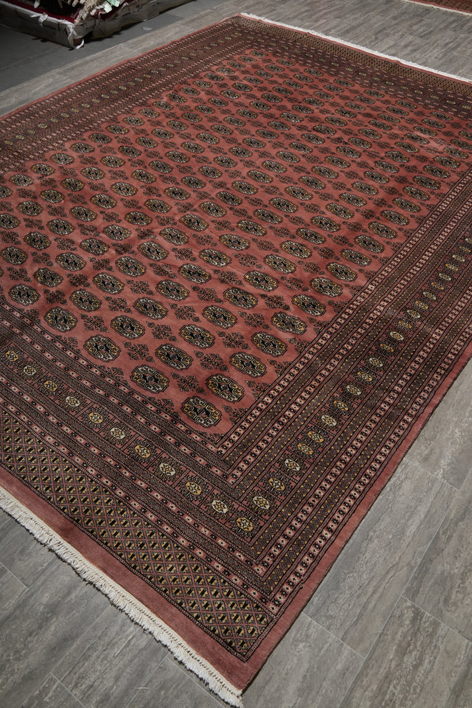 A traditional Persian-style area rug with a dusty red field, dark brown borders, and intricate black and gold medallion patterns, shown on a gray wood-look floor.