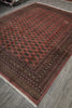 Load image into Gallery viewer, A traditional Persian-style area rug with a dusty red field, dark brown borders, and intricate black and gold medallion patterns, shown on a gray wood-look floor.