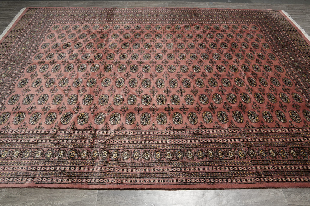 A large rectangular area rug with a dusty rose pink field, featuring rows of circular medallions and a detailed patterned border, laid out on a gray tiled floor.