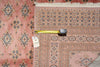 Load image into Gallery viewer, A pink patterned area rug with a geometric border design, shown folded with a yellow tape measure and a white inventory tag on top.