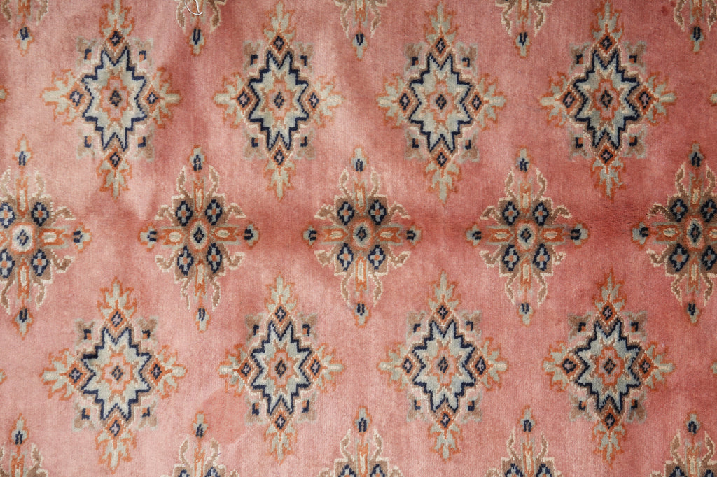 A close-up of a pink patterned fabric or rug featuring repeating geometric medallion motifs in navy blue, beige, and muted orange.