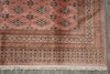 Load image into Gallery viewer, A close-up of a traditional patterned rug corner, showing a dusty pink field with repeating diamond motifs and ornate borders in beige, navy, and rust, finished with cream fringe.