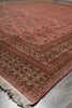 Load image into Gallery viewer, A traditional oriental rug with a dusty rose pink field, detailed geometric borders, and cream fringe, shown laid out on a gray floor.