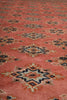 Load image into Gallery viewer, A close-up of a patterned textile or rug with a dusty coral-pink base and repeating geometric medallion motifs in navy, beige, and rust orange.