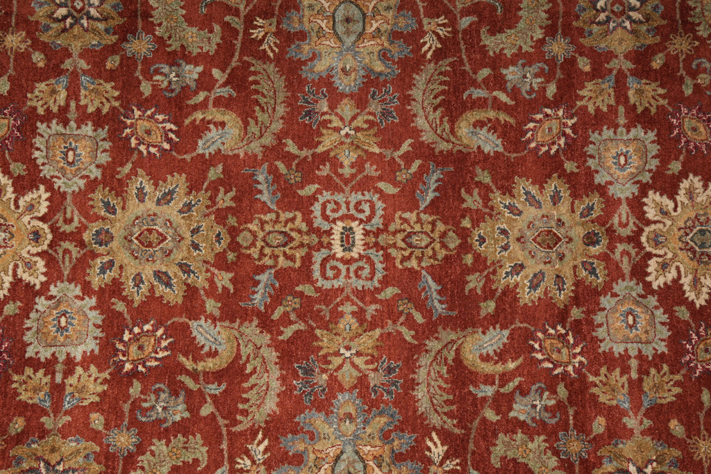 A close-up of an ornate patterned rug with a deep red background and intricate floral motifs in beige, gold, and muted blue.