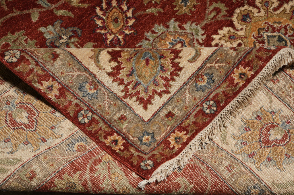 A folded traditional oriental rug with an intricate floral and geometric pattern in red, beige, blue, and brown tones, showing its woven texture and fringe detail.