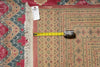 Load image into Gallery viewer, A traditional patterned area rug with cream, red, and blue geometric designs, shown with a yellow tape measure and a product tag on top to indicate scale.