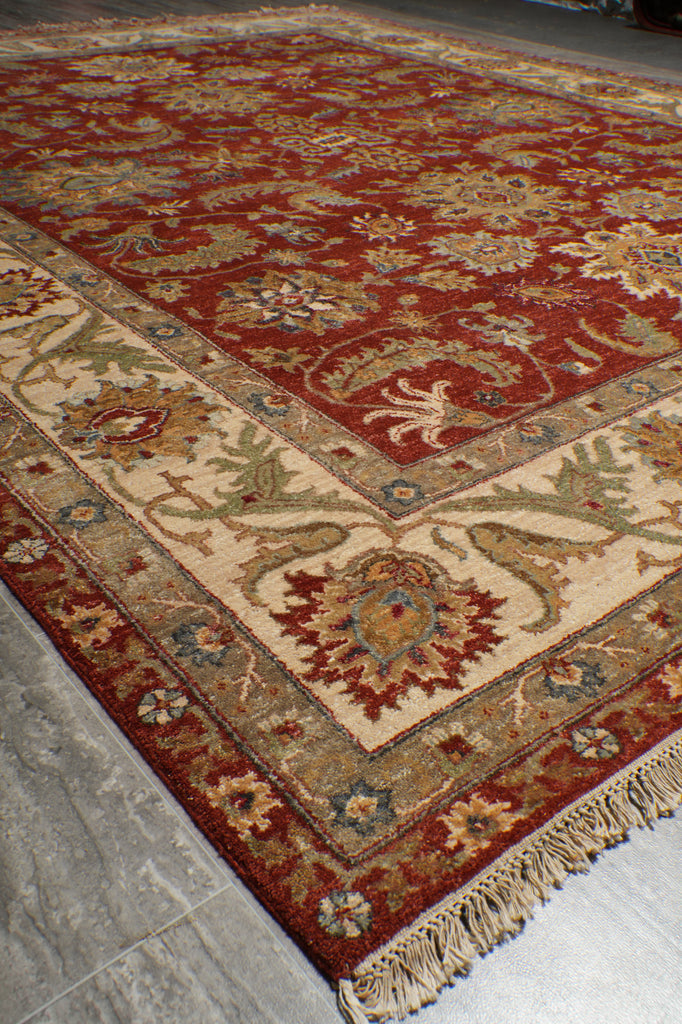 A traditional oriental area rug with a deep red field, beige border, and intricate floral motifs in blue, green, and gold, shown on a gray tiled floor.