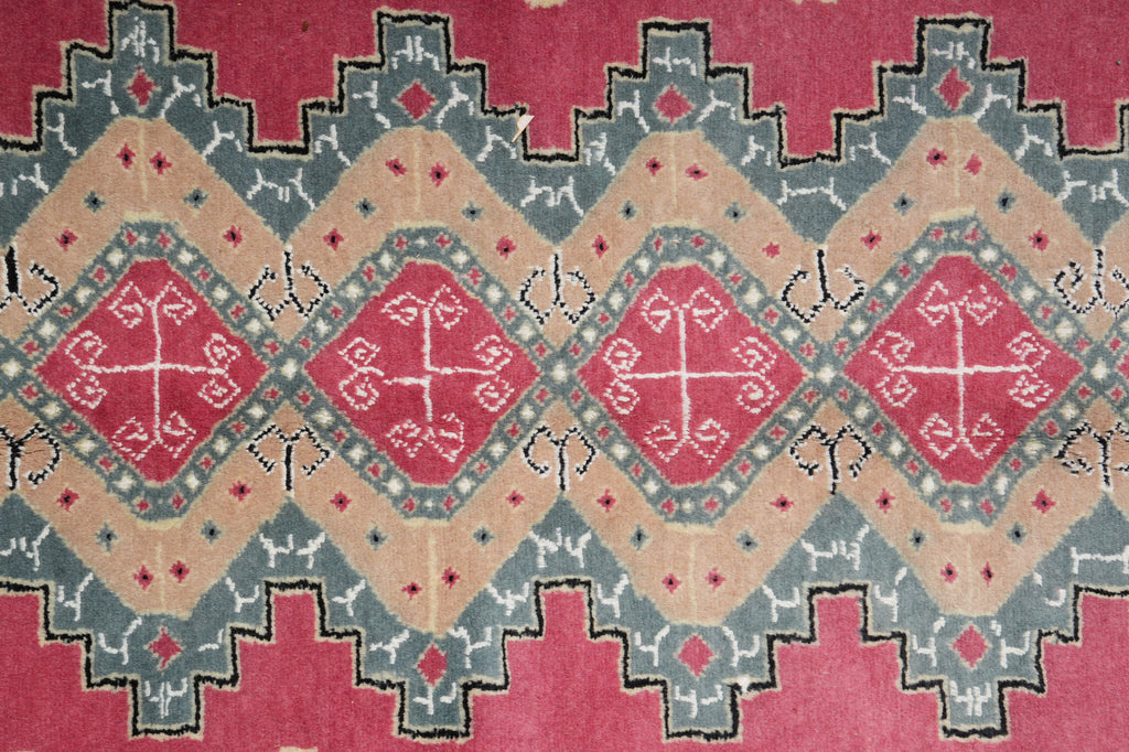 A close-up of a patterned rug featuring a geometric design with red diamond medallions, beige sections, and gray stepped borders.