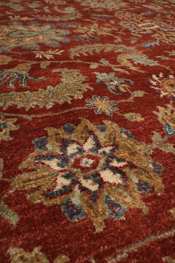 A close-up of a traditional patterned area rug with a deep red background and ornate floral motifs in beige, blue, and gold.