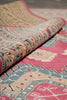 Load image into Gallery viewer, A close-up of a rolled section of a traditional patterned rug, showing its detailed woven design in pink, beige, blue, and red tones.