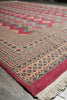 Load image into Gallery viewer, A close-up of a patterned rug with cream, red, and blue geometric motifs and a fringed edge, photographed on a gray floor.