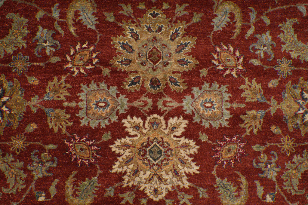 A close-up of a traditional patterned rug with a deep red background and ornate floral motifs in beige, blue, and gold.