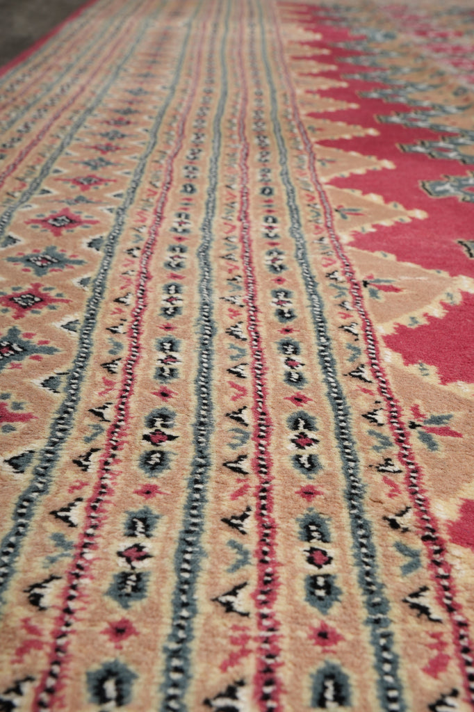 Close-up of a patterned rug with horizontal bands of geometric and tribal motifs in beige, red, blue, and black.