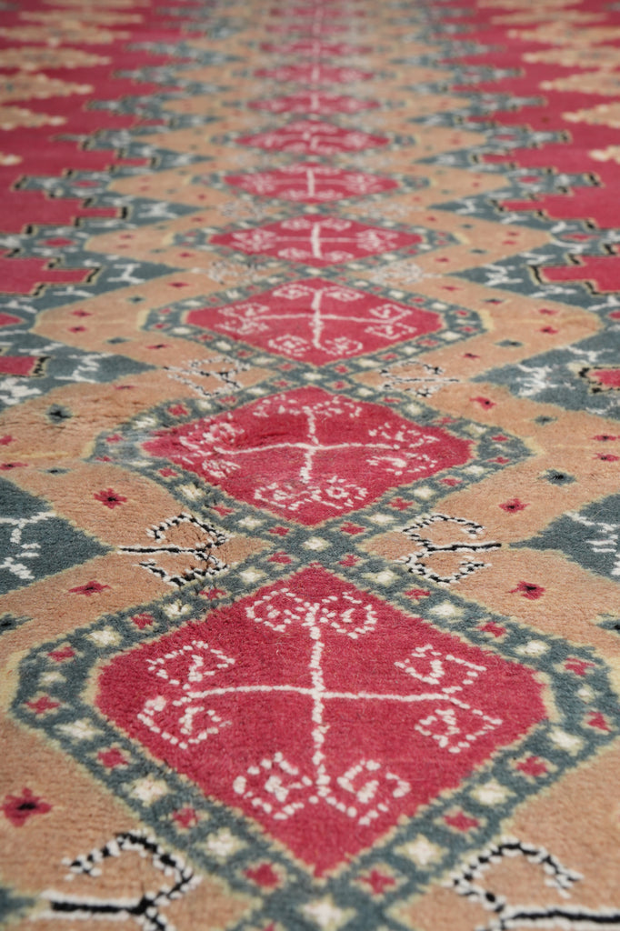 A close-up of a patterned textile or rug showing repeating diamond motifs in red, beige, gray, and black.