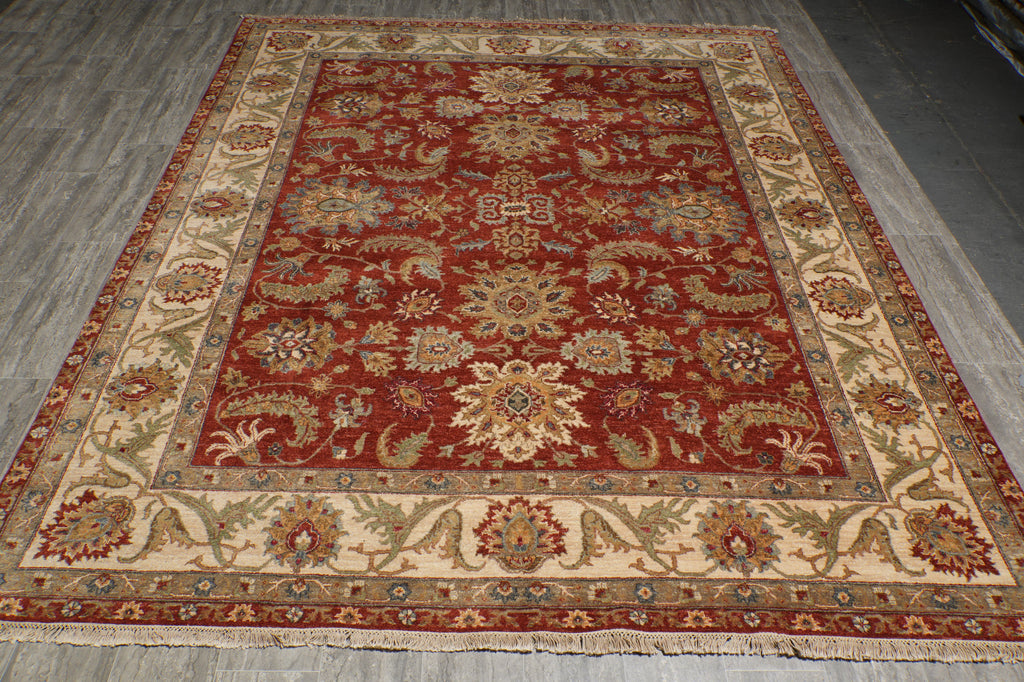 A traditional oriental area rug with a deep red central field, beige borders, and intricate floral motifs in blue, green, and gold, laid out on a gray wood floor.