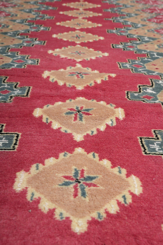 A close-up of a patterned rug featuring a deep red background with large beige diamond medallions and blue accents.